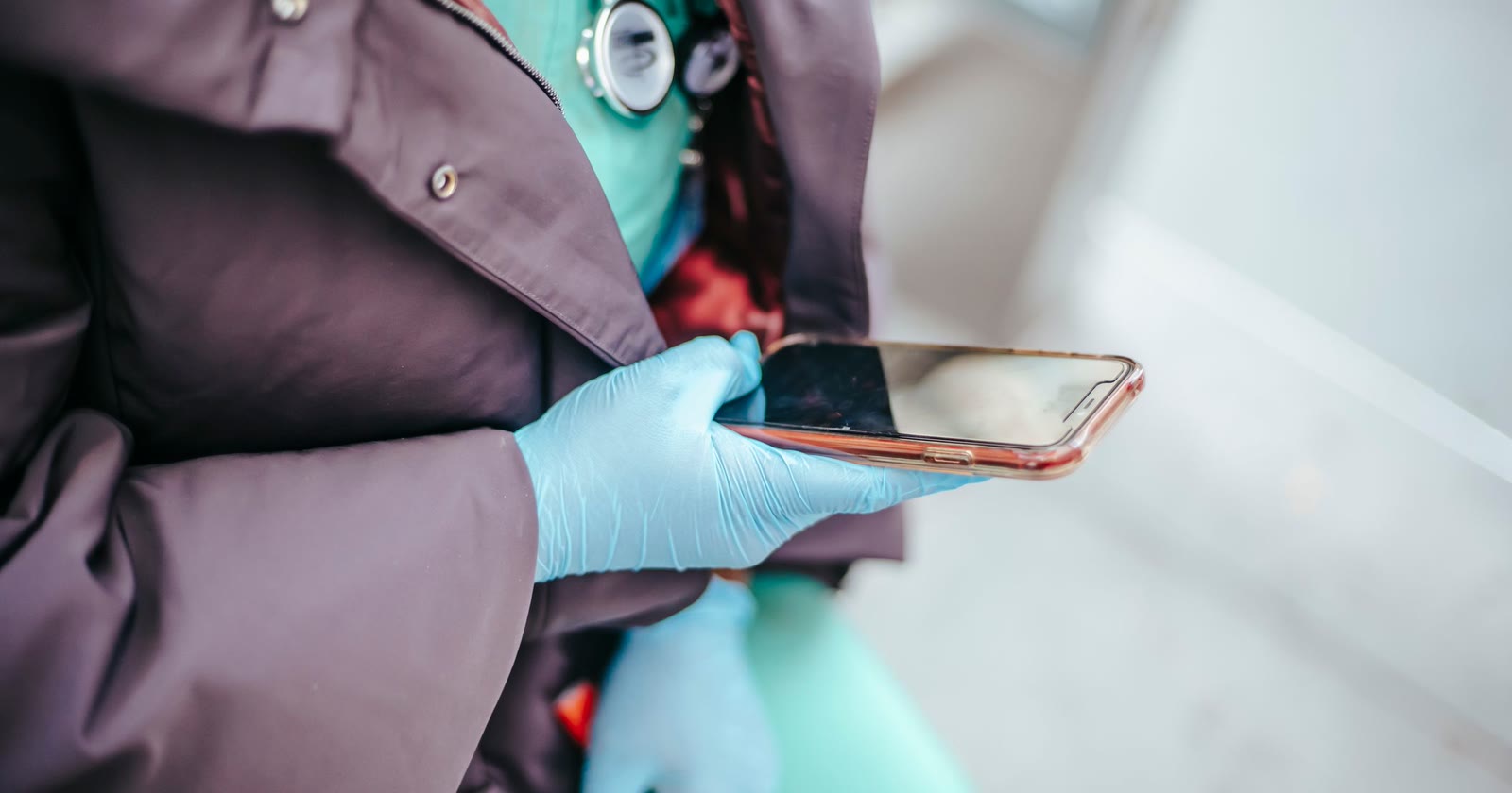 Profissional de saúde com estetoscópio no pescoço e luvas azuis segurando um celular